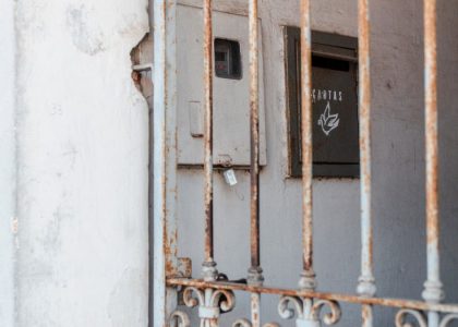 A rusty metal fence frames an old mail drop against a worn wall, creating a rustic atmosphere.