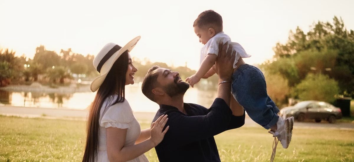 A joyful family moment with parents and child in a sunny park setting.