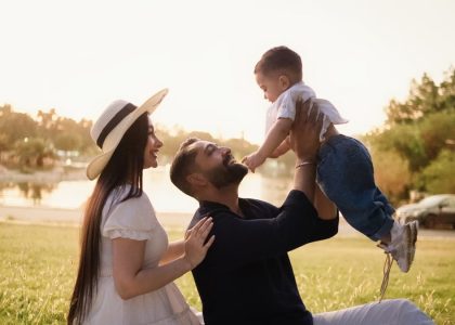 A joyful family moment with parents and child in a sunny park setting.
